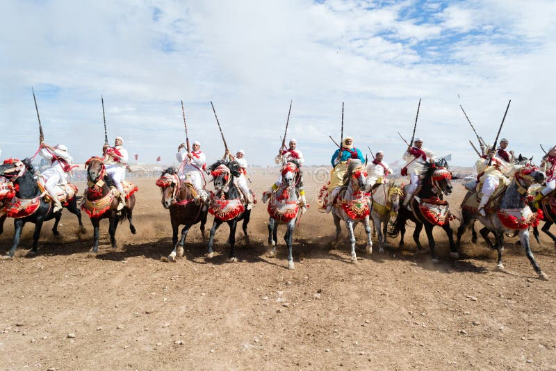 A close-up shot of a Fantasia rider, clad in traditional attire, firing an antique rifle while riding a horse during a Tbourida performance